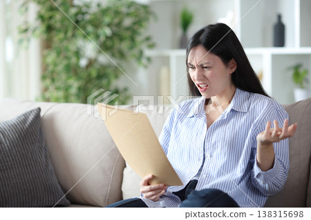 Angry asian woman reading paper document at home Angry asian woman reading paper document at home 138315698