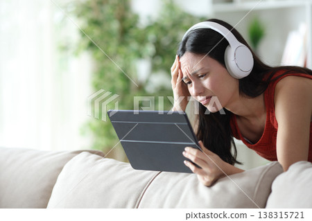 Worried asian woman watching online media on tablet Worried asian woman watching online media on tablet 138315721