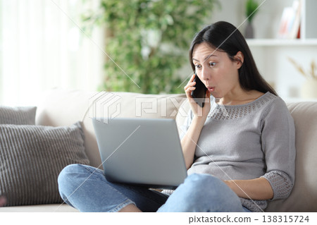 Surprised asian woman talking on phone using laptop at home 138315724
