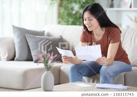 Satisfied asian woman reading paper letter at home 138315743