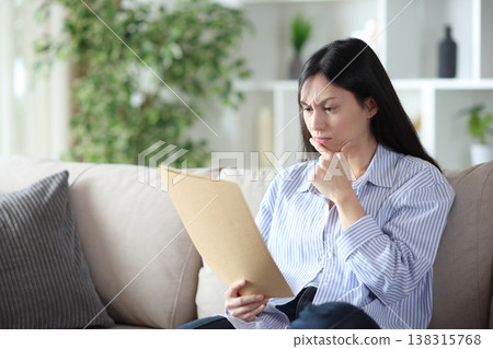 Suspicious asian woman reading form at home Suspicious asian woman reading form at home 138315768