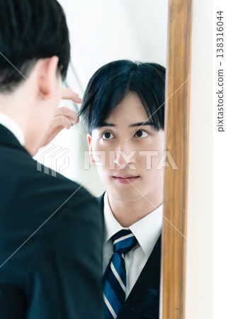 A man in a suit adjusts his appearance in front of a mirror. A man in a suit adjusts his appearance in front of a mirror. 138316044