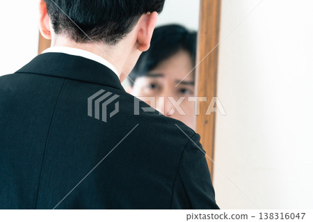 A man in a suit adjusts his appearance in front of a mirror. 138316047