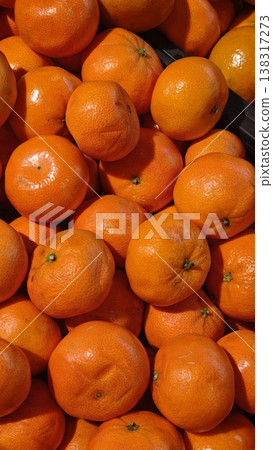 Fresh oranges piled together in a market display, showcasing vibrant orange color and textured skin, with a focus on their natural shine and freshness 138317273
