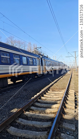 Electric train traveling along railway tracks under a clear blue sky, showcasing the side view of the train and the surrounding landscape Electric train traveling along railway tracks under a clear blue sky, showcasing the side view of the train and the surrounding landscape 138317316