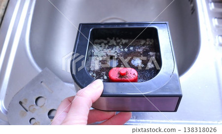 A coffee machine drip tray positioned over an empty metal sink; inside the tray,which belongs to a home coffee machine,lie remnants of coffee grounds, covered in fungus and mold 138318026