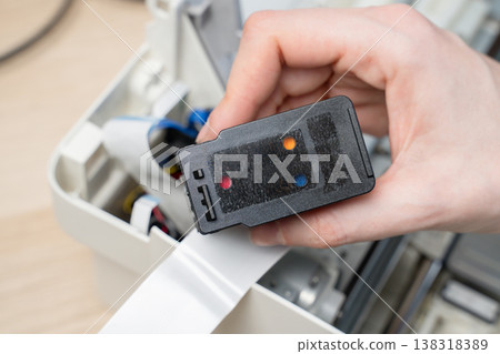 Close-up of a hand removing an ink cartridge from the interior of a printer during maintenance or repair, showing ribbon cable, wiring and mechanical components in a small workspace setting. Close-up of a hand removing an ink cartridge from the interior of a printer during maintenance or repair, showing ribbon cable, wiring and mechanical components in a small workspace setting. 138318389