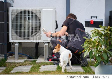 Technician servicing outdoor heat pump unit near house 138319267