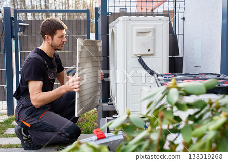 Technician servicing outdoor air source heat pump unit near house wall Technician servicing outdoor air source heat pump unit near house wall 138319268