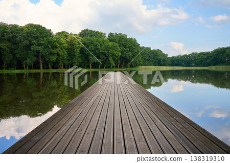 Wooden pier on calm lake surrounded by green trees 138319310