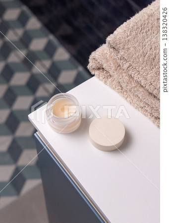 Opened handmade lip balm jar in blue bathroom with towel. Blank lid cosmetic mockup 138320426
