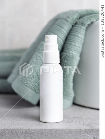 White spray bottle mockup near sage green bath towel in bathroom. Unbranded cosmetic packaging White spray bottle mockup near sage green bath towel in bathroom. Unbranded cosmetic packaging 138320441