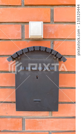 Black metal mailbox and a white doorbell button on a vibrant red brick wall of a house entrance 138320444