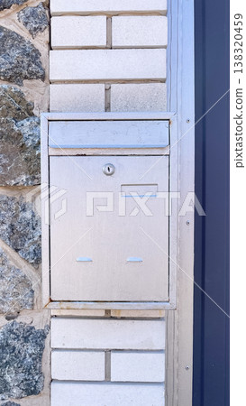 Silver metal mailbox mounted on a rustic stone wall next to a blue corrugated fence in daylight Silver metal mailbox mounted on a rustic stone wall next to a blue corrugated fence in daylight 138320459