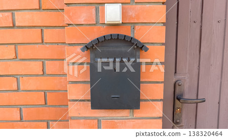 Traditional black metal mailbox on a red brick wall next to a brown door with a handle and doorbell Traditional black metal mailbox on a red brick wall next to a brown door with a handle and doorbell 138320464