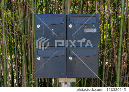 Black outdoor mailbox unit with multiple compartments installed on wooden post near bamboo fence residential mail system 138320645