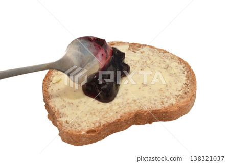 Spread jam on a slice of buttered bread with a spoon. 138321037