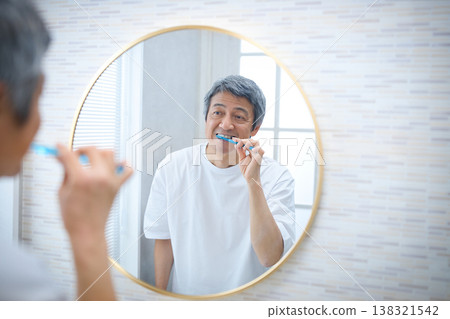 一位 60 多歲的男子一邊刷牙一邊照鏡子 138321542