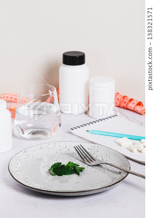 Parsley leaves and a fork on an empty plate, a notebook and capsules on the table vertical view Parsley leaves and a fork on an empty plate, a notebook and capsules on the table vertical view 138321571