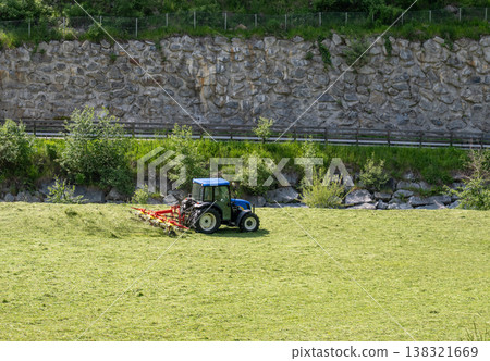 Blue tractor mowing grass field with agricultural machinery farming landscape rural work concept 138321669