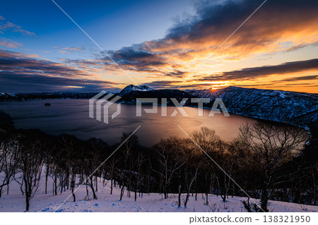 The snow-covered forest and Lake Mashu at dawn: A breathtaking winter landscape bathed in orange light. 138321950