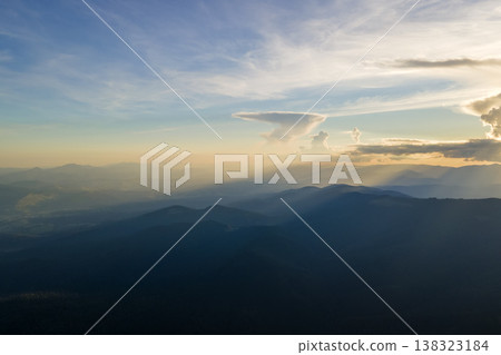 Aerial view of dark mountain hills with bright sunrays of setting sun at sunset. Hazy peaks and misty valleys in evening Aerial view of dark mountain hills with bright sunrays of setting sun at sunset. Hazy peaks and misty valleys in evening 138323184