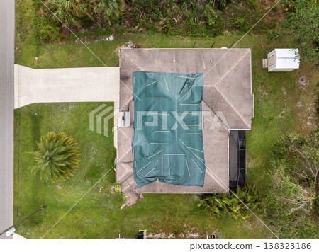 Aerial view of damaged in hurricane house roof covered with blue protective tarp against rain water leaking until replacement of asphalt shingles Aerial view of damaged in hurricane house roof covered with blue protective tarp against rain water leaking until replacement of asphalt shingles 138323186