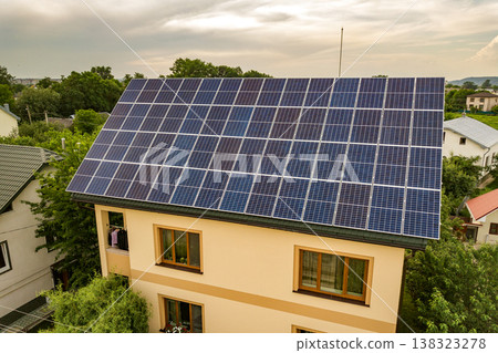 Aerial top view of new modern residential house cottage with blue shiny solar photo voltaic panels system on roof. Renewable ecological green energy production concept. Aerial top view of new modern residential house cottage with blue shiny solar photo voltaic panels system on roof. Renewable ecological green energy production concept. 138323278