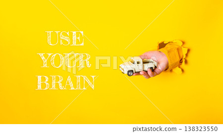 Hand holding a toy truck breaking through a vibrant yellow background, symbolizing creativity and imagination in business and marketing strategies for innovative thinking 138323550