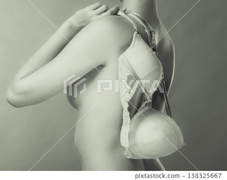 Naked woman holds beige bra in hand Naked woman holds beige bra in hand 138325667