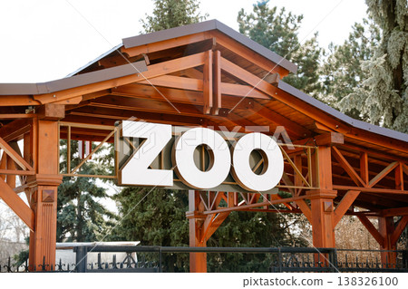 Zoo entrance sign mounted on wooden structure with large bold letters surrounded by trees creating welcoming outdoor setting for visitors 138326100