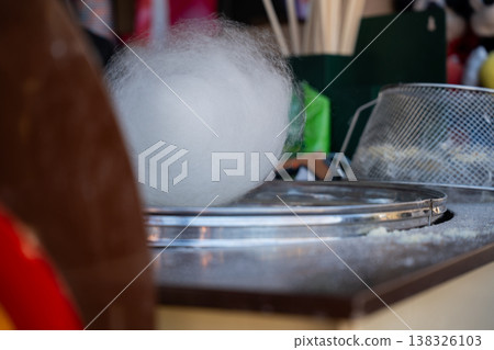 Fresh cotton candy being spun on machine at fair stall creating fluffy white sweet treat with sugar threads in motion at carnival food stand 138326103