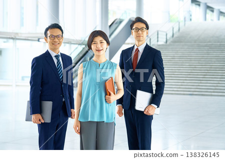 三位商務團隊成員，兩男一女，在辦公大樓入口處微笑。 138326145