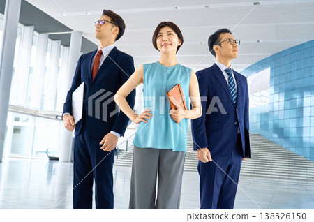 A business team of three men and women, standing confidently in the office, looking towards the future. 138326150