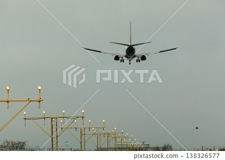 Airplane approaching landing on runway with illuminated approach lights under overcast sky, showcasing aviation infrastructure and flight operations in action Airplane approaching landing on runway with illuminated approach lights under overcast sky, showcasing aviation infrastructure and flight operations in action 138326577