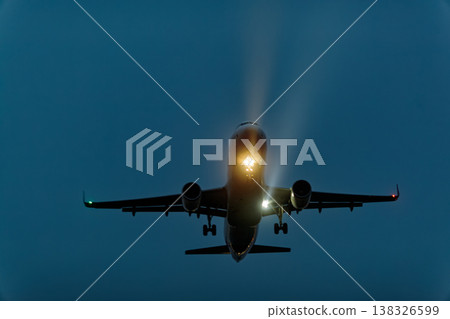 Airplane approaching for landing at dusk with landing lights illuminated, showcasing the aircraft's silhouette against a darkening sky 138326599