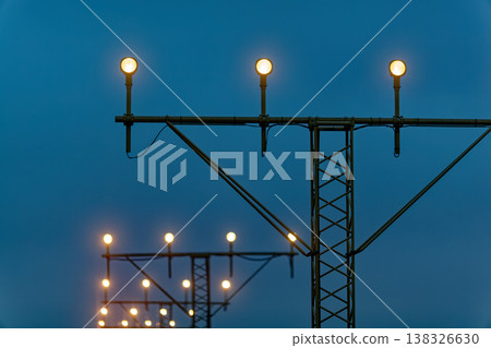 Series of illuminated airport runway lights on tall poles against a twilight sky, highlighting the structure and arrangement of the lighting system 138326630