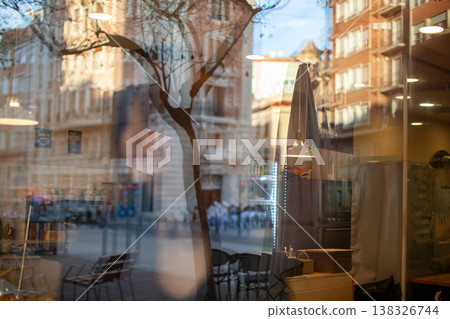 Reflection of a tree and people in a cafe window, showcasing urban architecture and outdoor seating in a vibrant city street setting 138326744