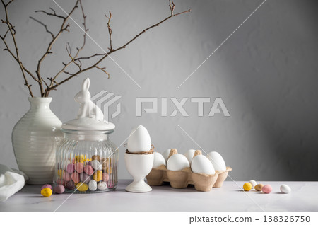 Easter background, table with spring decorations: eggs, candies, twigs in a vase and egg candies. Easter background, table with spring decorations: eggs, candies, twigs in a vase and egg candies. 138326750