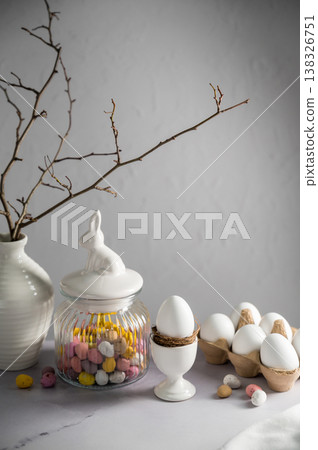 Easter background, table with spring decorations: eggs, candies, twigs in a vase and egg candies. Easter background, table with spring decorations: eggs, candies, twigs in a vase and egg candies. 138326751