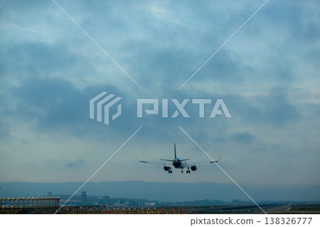 Airplane landing at airport runway during twilight with clouds in the sky and airport buildings visible in the background Airplane landing at airport runway during twilight with clouds in the sky and airport buildings visible in the background 138326777