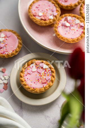 Valentine's day. Pink mini tarts with heart shaped sprinkles, cup of coffee and bouquet of spring red tulips Valentine's day. Pink mini tarts with heart shaped sprinkles, cup of coffee and bouquet of spring red tulips 138326808