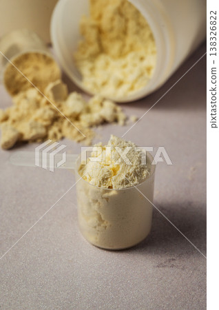 Protein powder in scoops with white plastic protein tubes, jars in background. Body building, muscle growth and food supplement concept Protein powder in scoops with white plastic protein tubes, jars in background. Body building, muscle growth and food supplement concept 138326822