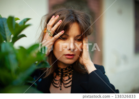 Female model with brown hair wearing black clothing and jewelry poses with hands on her head, surrounded by green foliage in an outdoor setting Female model with brown hair wearing black clothing and jewelry poses with hands on her head, surrounded by green foliage in an outdoor setting 138326833