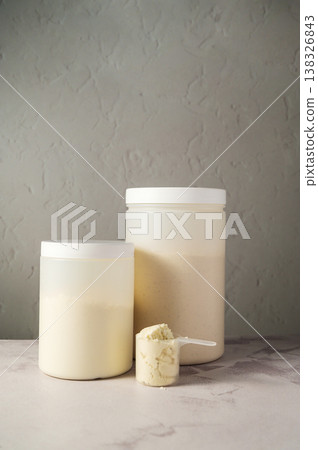 Protein powder in scoops with white plastic protein tubes, jars in background. Body building, muscle growth and food supplement concept Protein powder in scoops with white plastic protein tubes, jars in background. Body building, muscle growth and food supplement concept 138326843