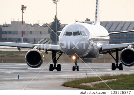 Commercial airplane taxiing on runway at airport with terminal buildings and control tower visible in the background during daylight hours Commercial airplane taxiing on runway at airport with terminal buildings and control tower visible in the background during daylight hours 138326877