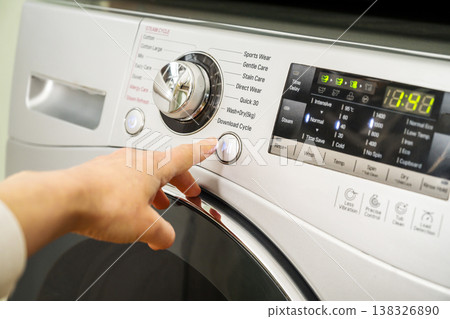 Washing machine. Pressing start button on modern washing machine display. Daily chores, close-up shot Washing machine. Pressing start button on modern washing machine display. Daily chores, close-up shot 138326890