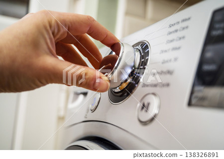 Smart home appliances. Adjusting washing machine setting. Hand turning the dial of a modern washing machine. Daily chores Smart home appliances. Adjusting washing machine setting. Hand turning the dial of a modern washing machine. Daily chores 138326891
