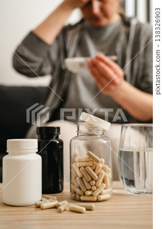 Medical treatment, jar with pills on the table and a woman on background measuring fever. Medical treatment, jar with pills on the table and a woman on background measuring fever. 138326903
