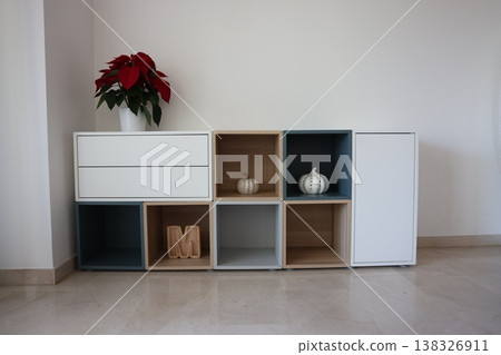 Modern wooden storage unit with white and blue compartments, featuring decorative pumpkins and a poinsettia plant on top in a bright indoor setting Modern wooden storage unit with white and blue compartments, featuring decorative pumpkins and a poinsettia plant on top in a bright indoor setting 138326911